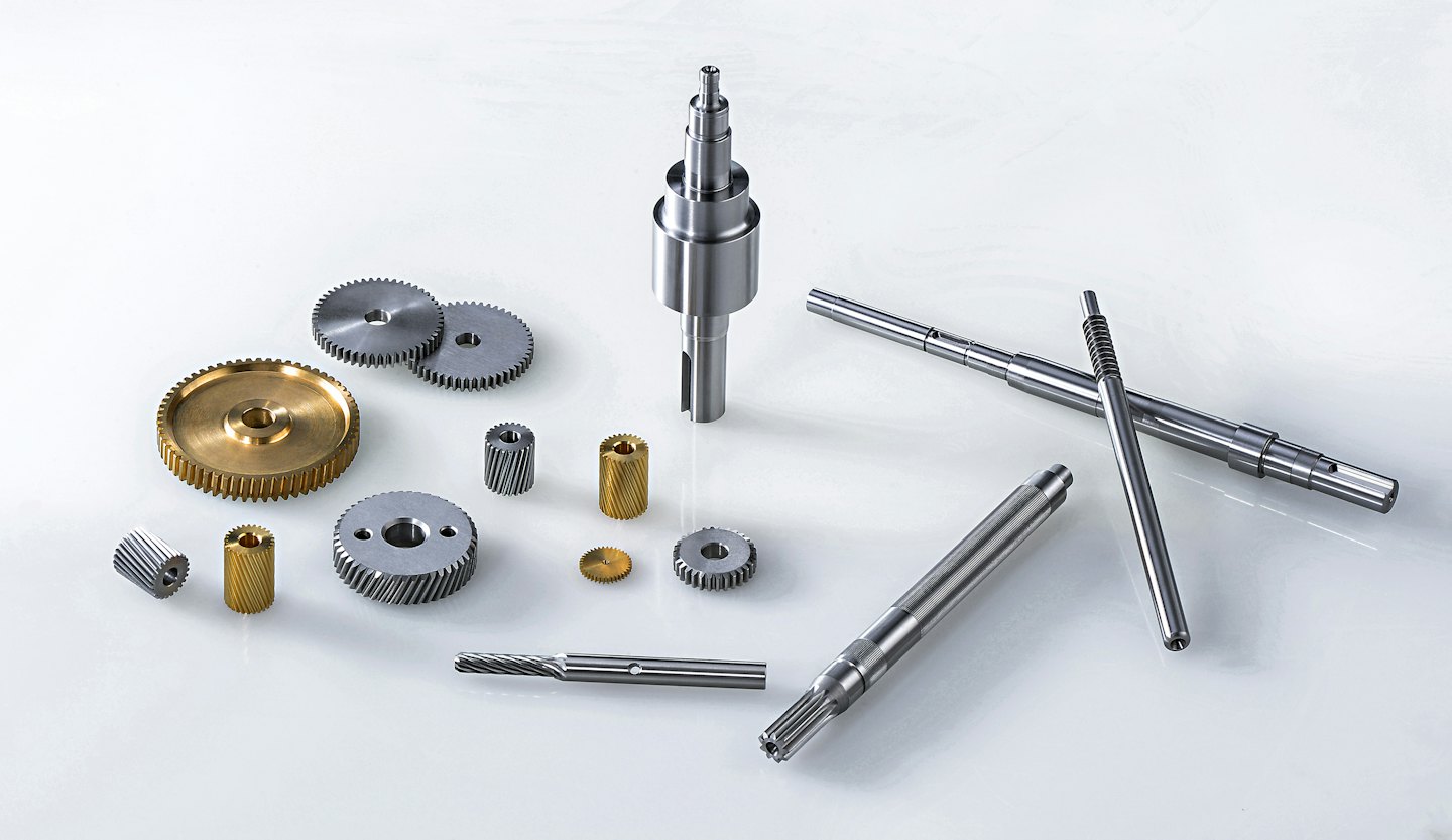 Verschiedene Metallzahnräder und Wellen auf weißem Untergrund.